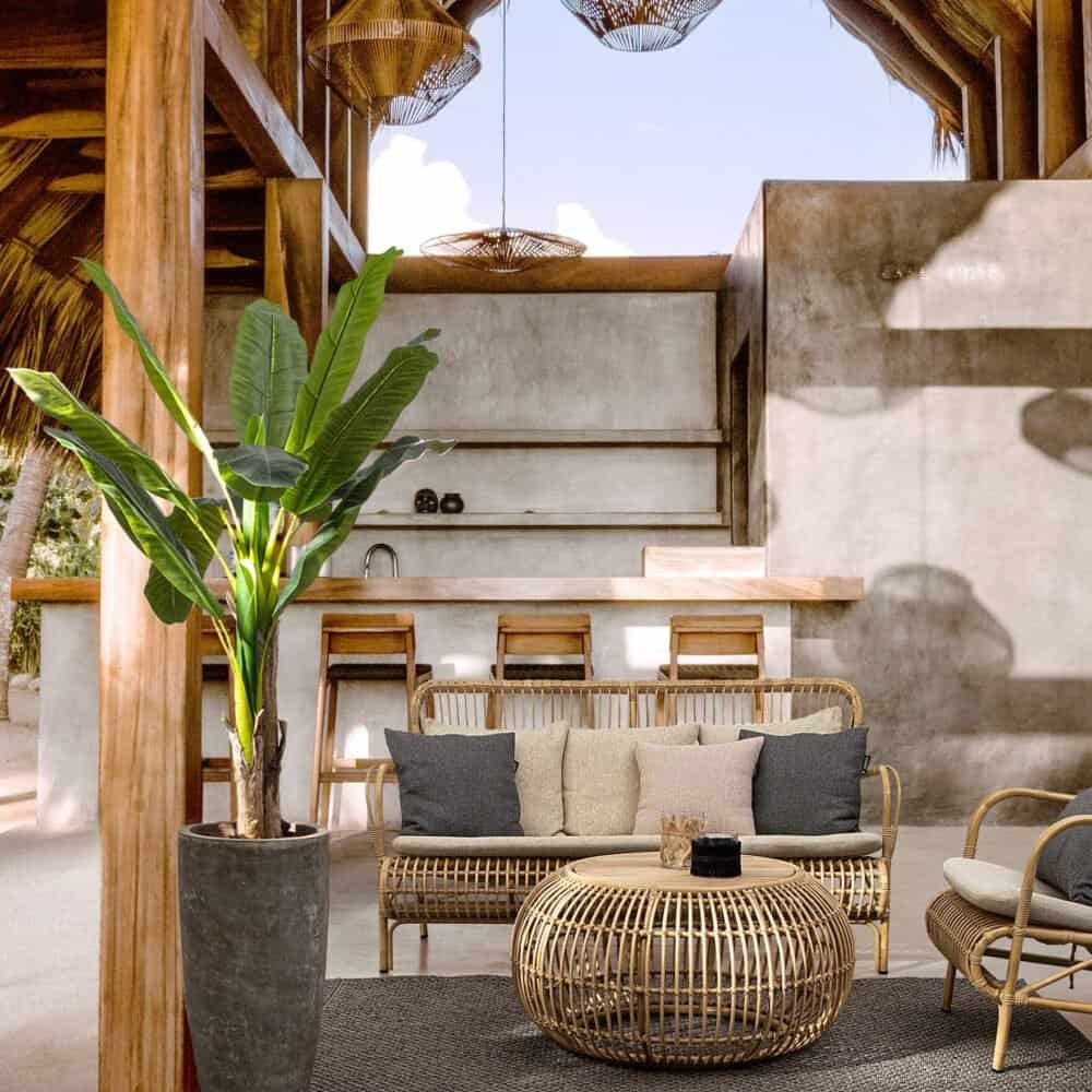 Soggiorno all'aperto con mobili in rattan, decorazioni in stile tropicale, e atmosfera rilassante.
