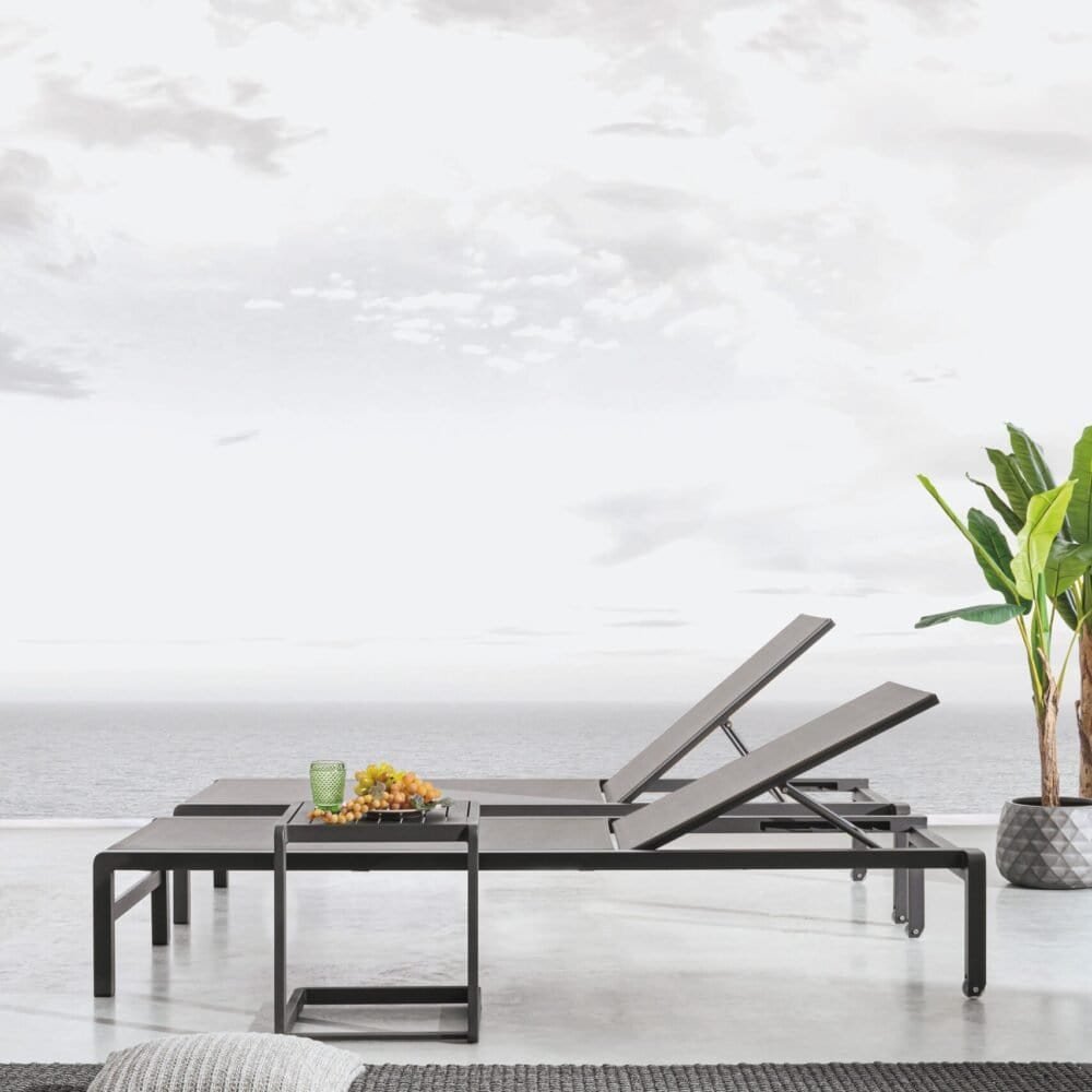 Sdraio nere con tavolino e piante tropicali, relax fronte mare, ambiente elegante e moderno.