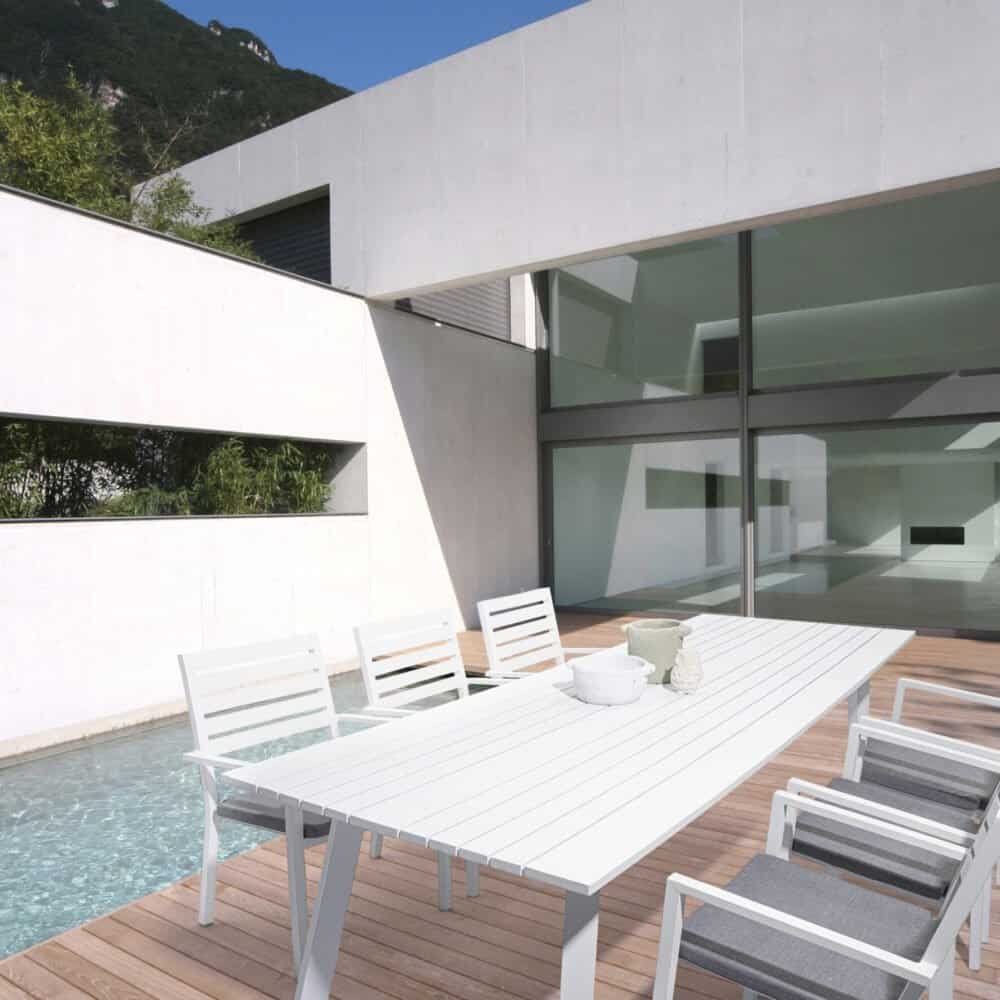 Tavolo da esterno in bianco con sedie in stile minimalista, piscina e arredamento di design su terrazza moderna.