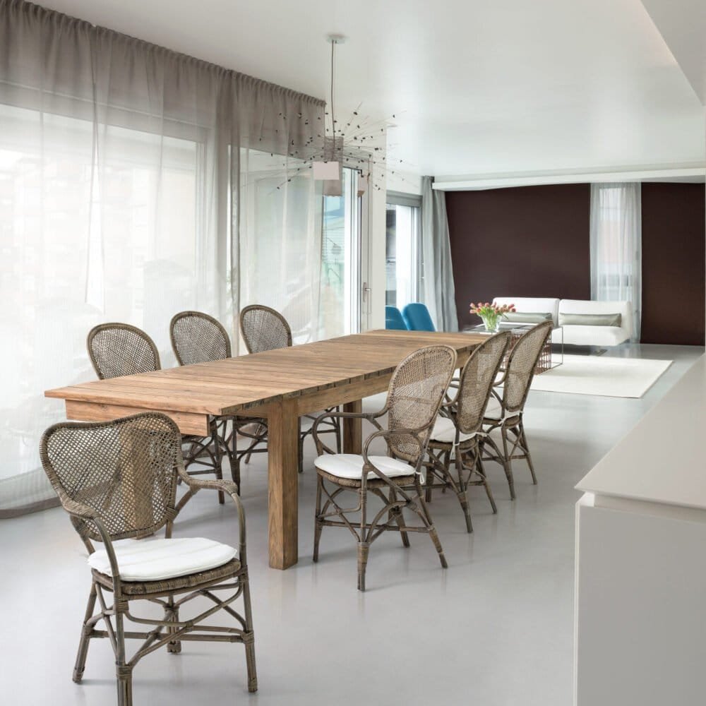 Sala da pranzo moderna con tavolo in legno e sedie in vimini, ambiente luminoso e accogliente.
