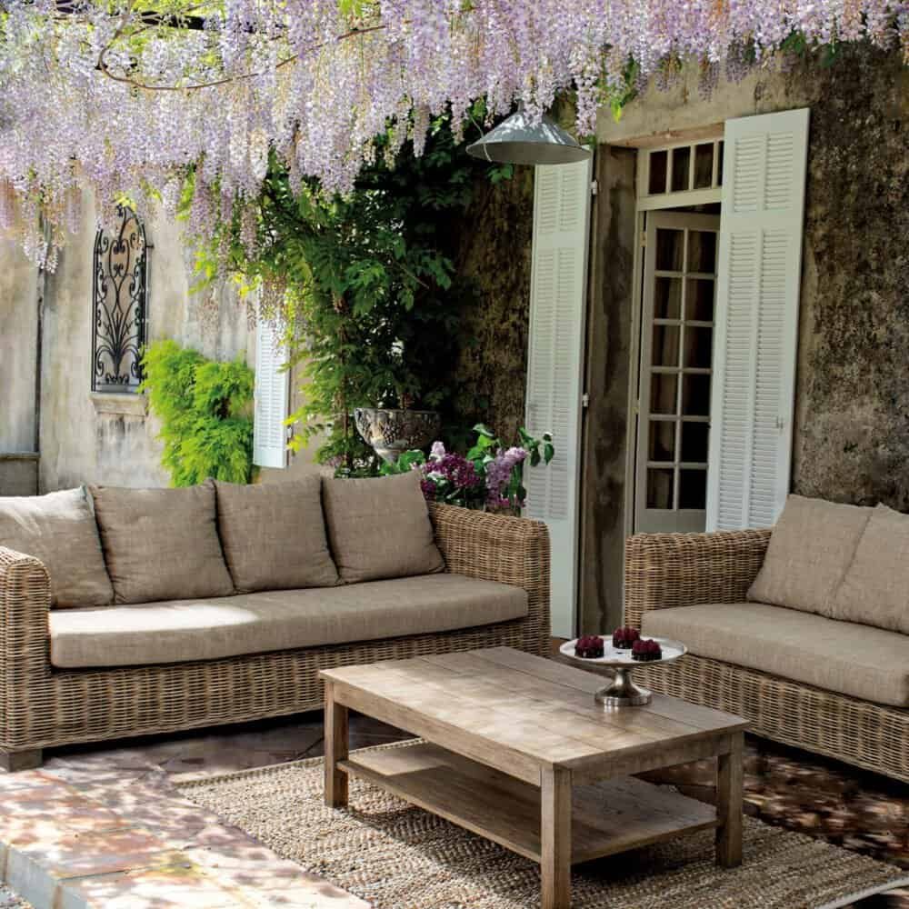 Soggiorno esterno con divani in vimini e decorazioni floreali in giardino.