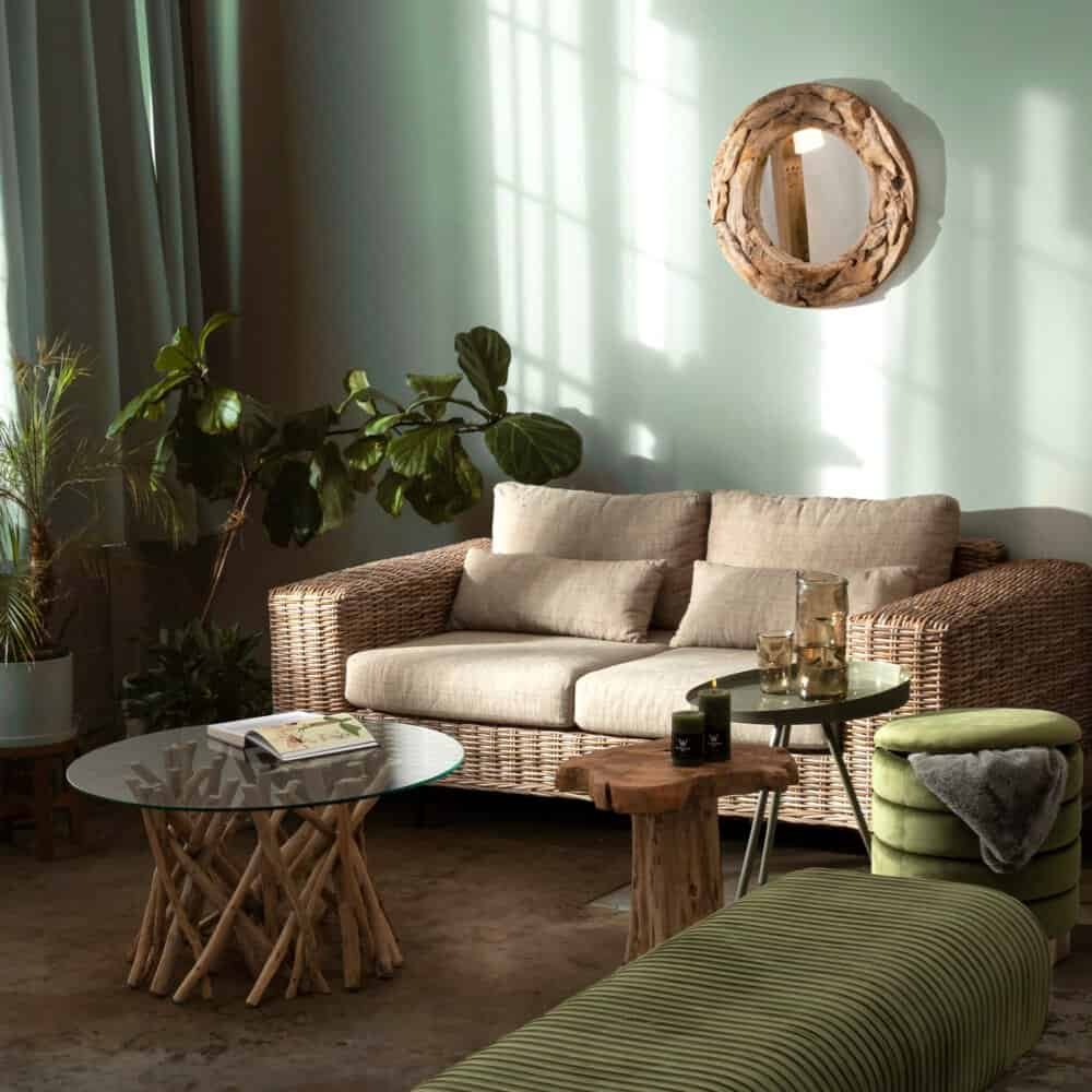 Soggiorno con divano in rattan, tavolini in legno e decorazioni rustiche, atmosfera accogliente e verde.