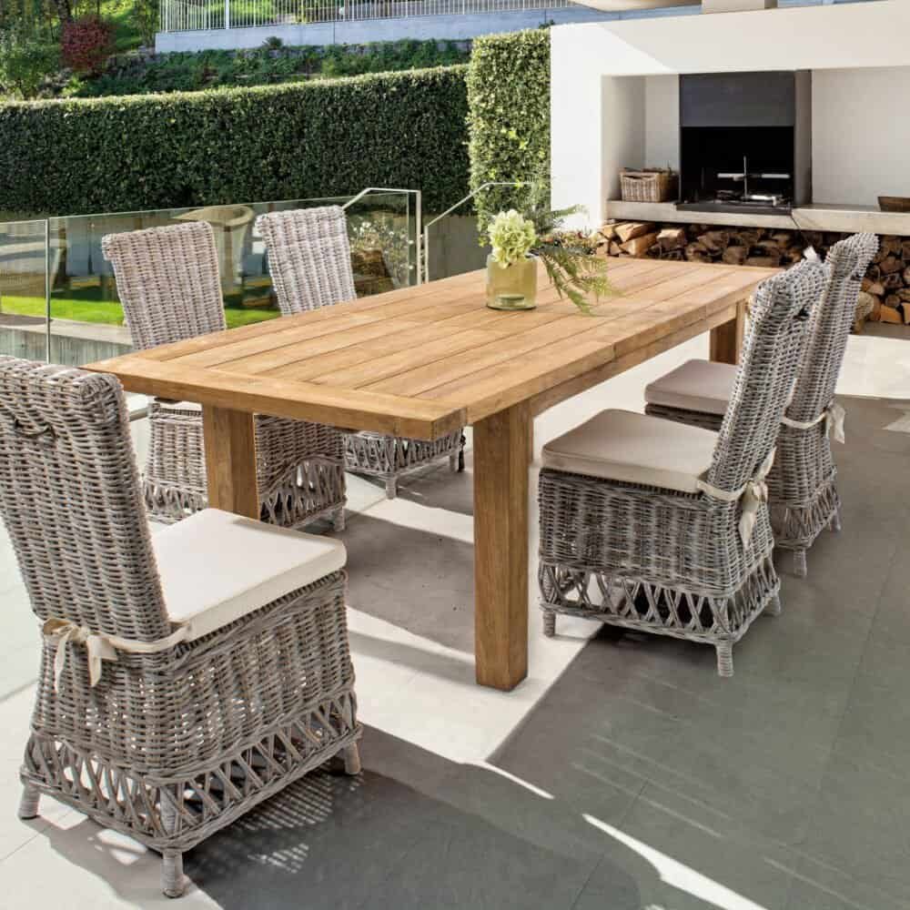 Spazio esterno con tavolo in legno e sedie in vimini, perfetto per pranzi e cene all'aperto in un ambiente elegante e confortevole.