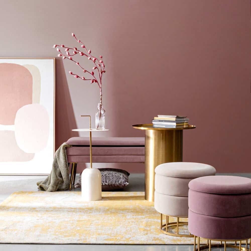 Vaso con ramoscello decorativo rosa e oro, tavolini in stile contemporaneo con oggetti di design.
