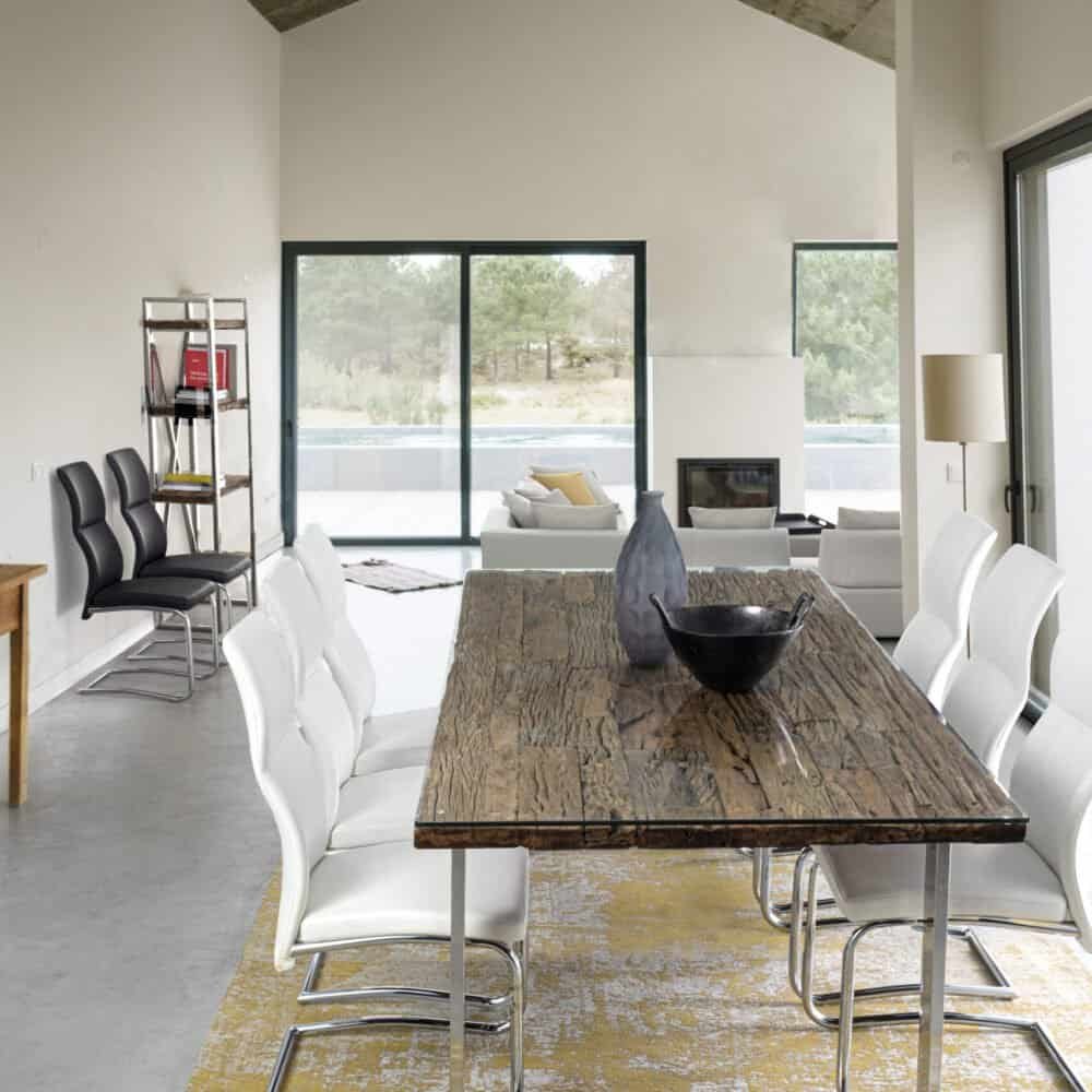 Ampio spazio living con tavolo in legno naturale, sedie bianche, e grande finestra scorrevole che offre vista panoramica e luce naturale.