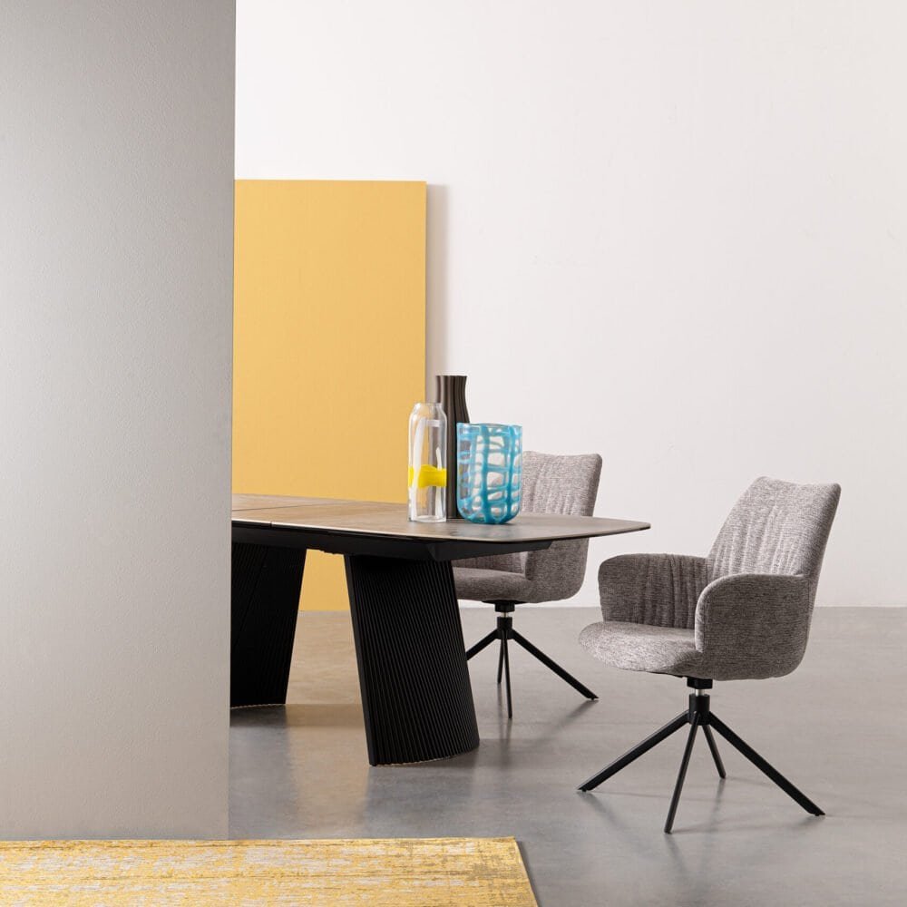 Sedia moderna in tessuto grigio con base nero, abbinata a tavolo di design in un ambiente minimalista.