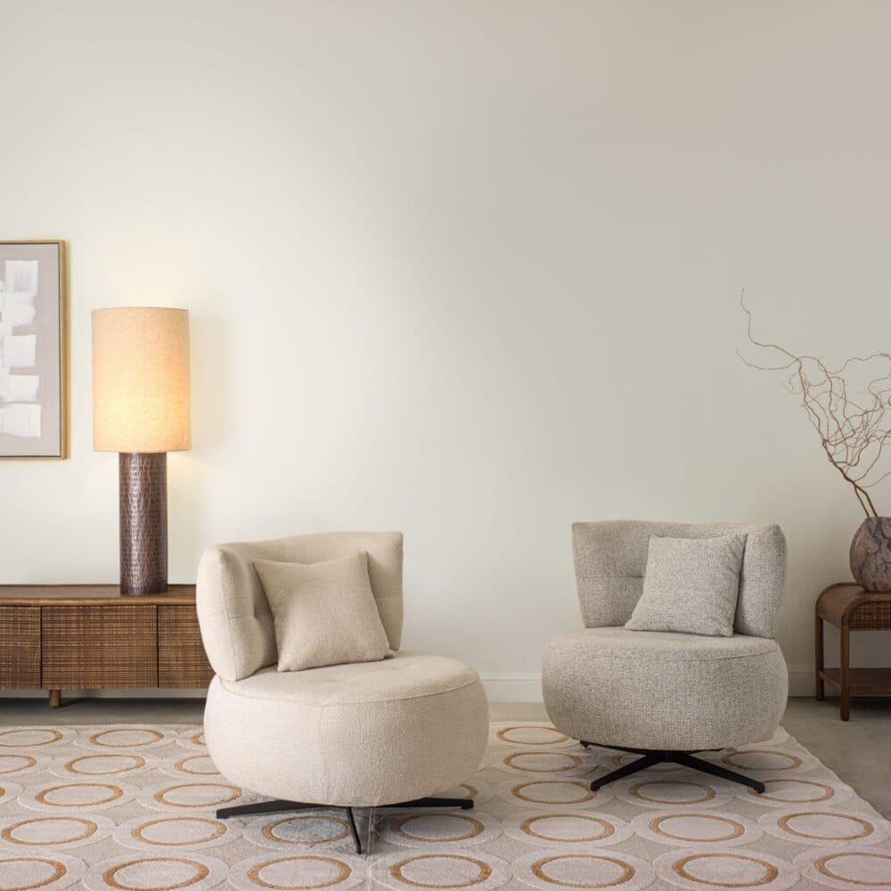 Elegante soggiorno minimalista con poltrone beige, lampada da tavolo e arredo moderno.