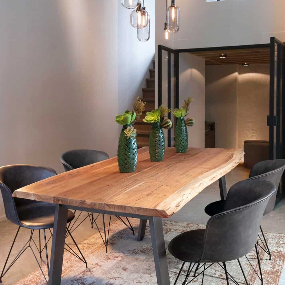 Elegante tavolo in legno naturale con sedie nere, decorato con vasi verdi, luce soffusa e arredi moderni, ideale per spazi raffinati.