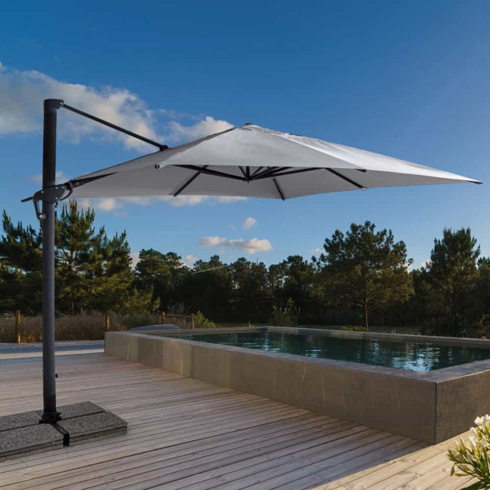 Ombrellone bianco sopra piscina all'aperto in un ambiente naturale con pini e cielo sereno.