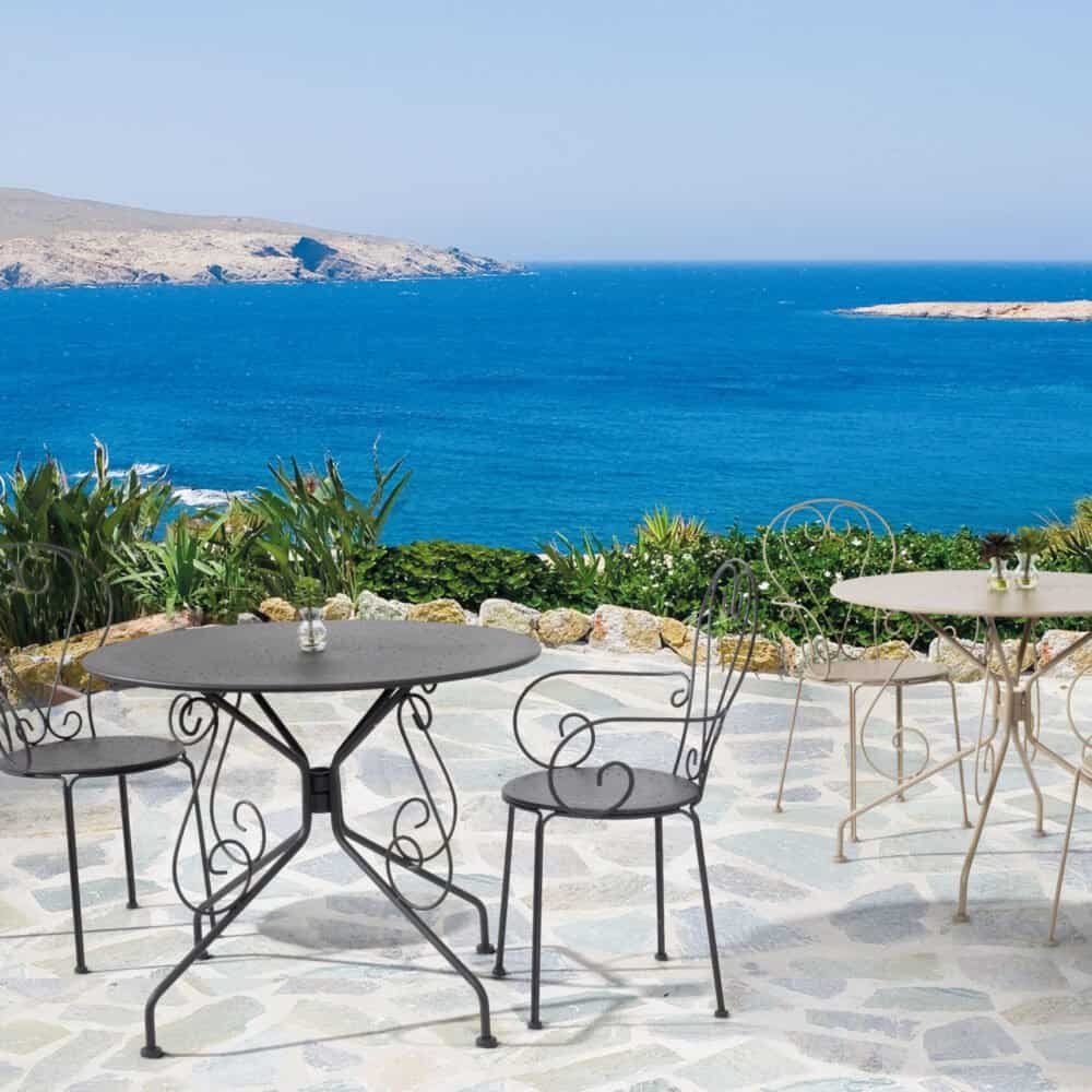 Tavoli in ferro battuto con vista mare sulla costa mediterranea, terrazza relax con piante e atmosfera romantica.