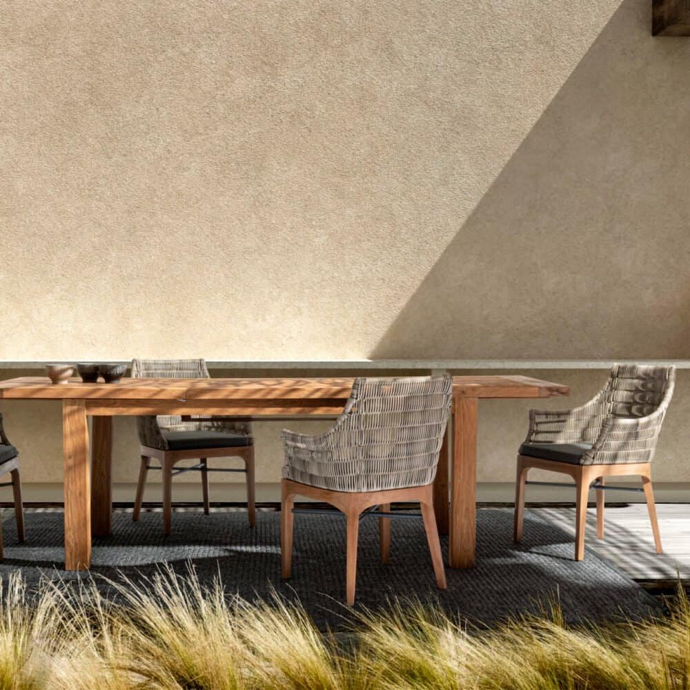Ampio tavolo da pranzo in legno con sedie in rattan, ideale per esterni, atmosfera di relax e stile contemporaneo.