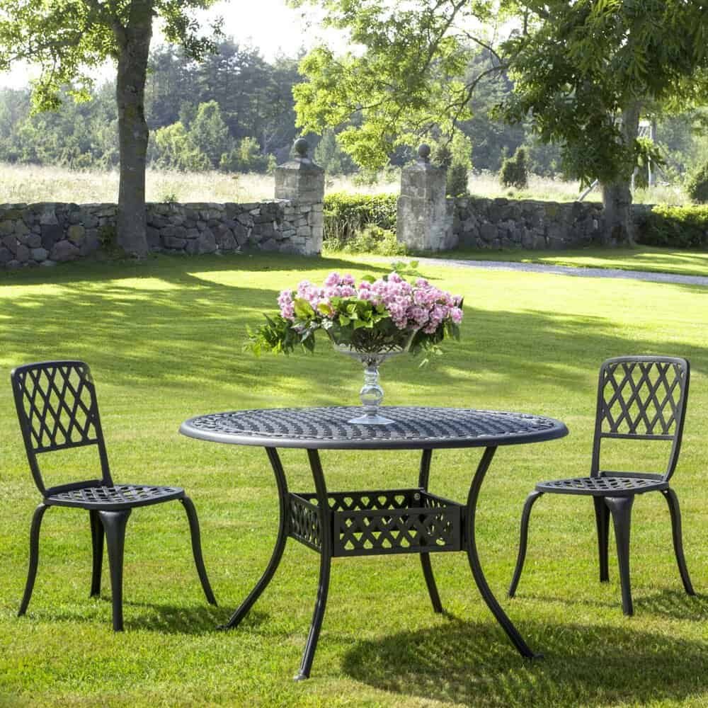 Tavolo e sedie di ghisa per giardini e balconi, con fiori rosa come decorazione esterna.