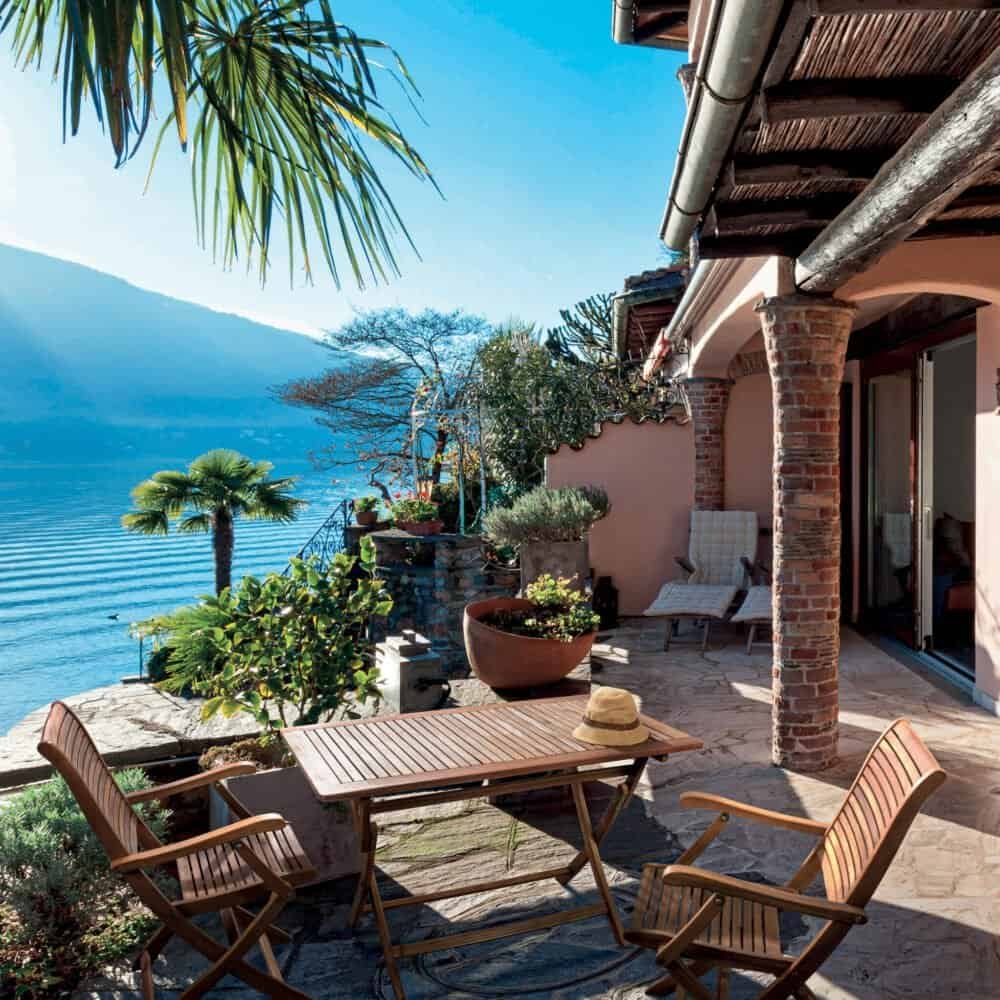 Tela vista di una terrazza con vista lago, piante, arredi in legno e atmosfera rilassante.