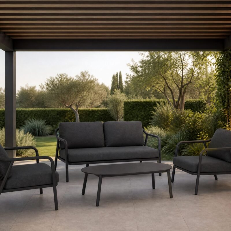Modern outdoor patio with dark gray cushioned seating under a wooden pergola, surrounded by greenery and a glass door on the right.