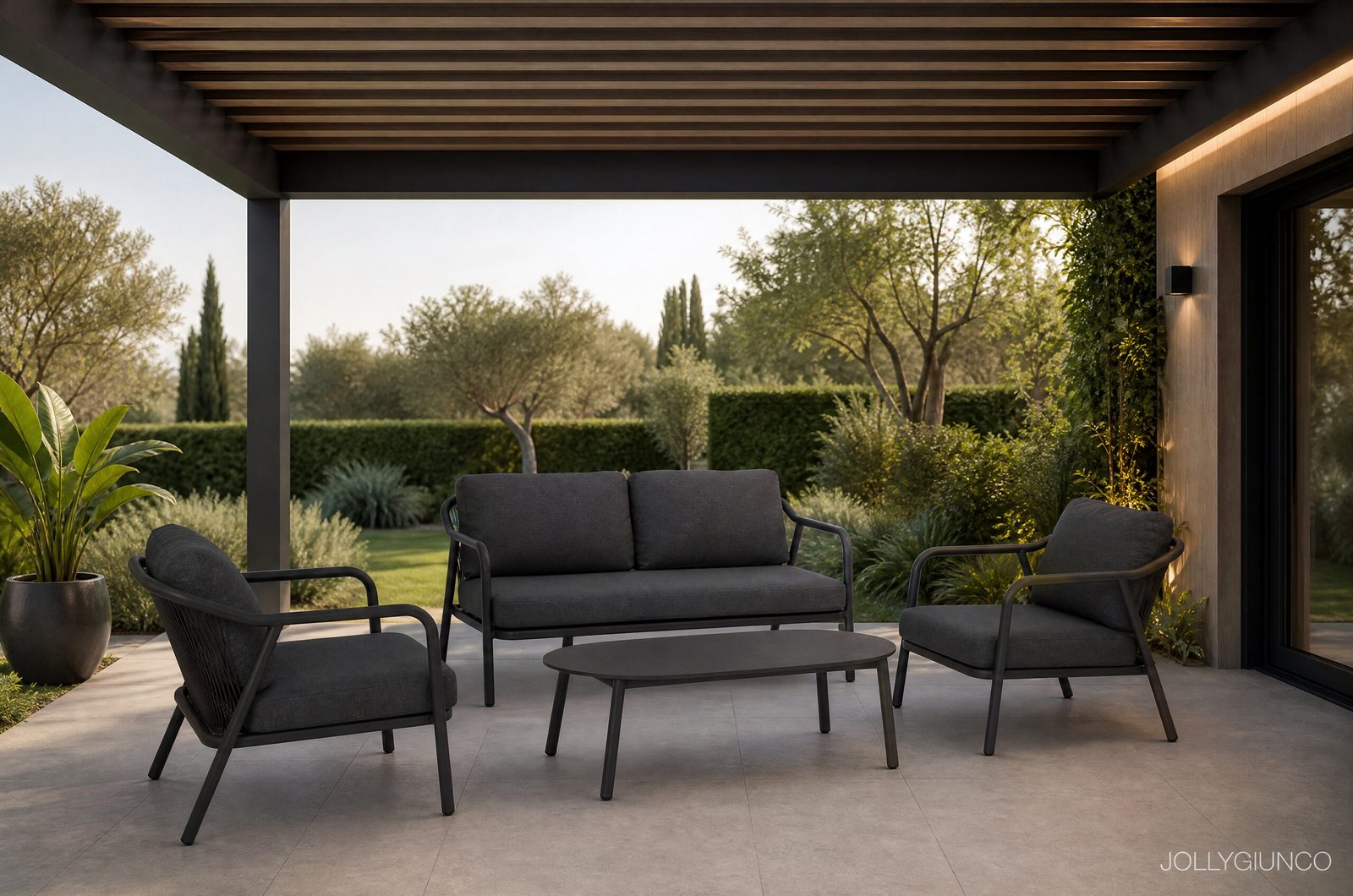 SET4 SALOTTO C-C MIRAVET ANT JA60-VERDE - JOLLYGIUNCO Modern outdoor patio with dark gray cushioned seating under a wooden pergola, surrounded by greenery and a glass door on the right.