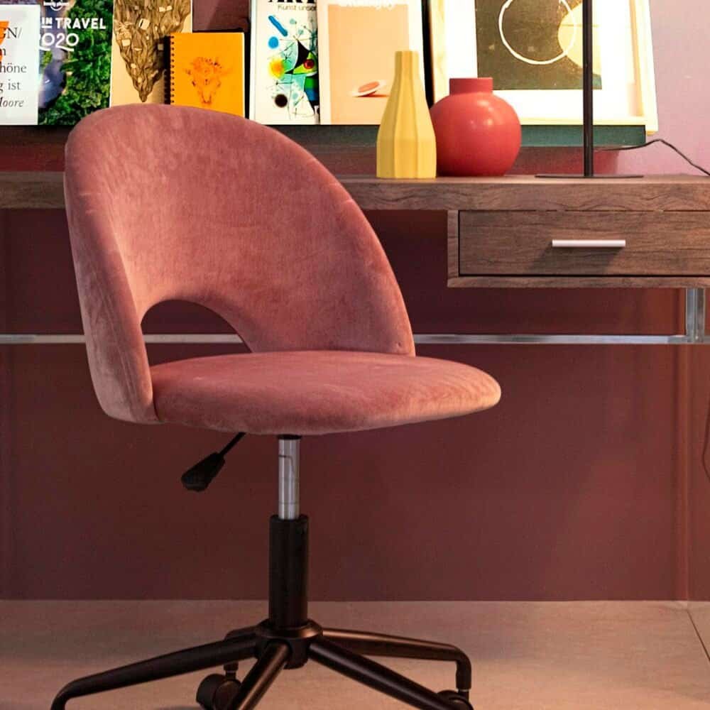 Alt text: Sedia rosa in velluto con schienale curvo, scrivania con decorazioni colorate e lampada moderna.