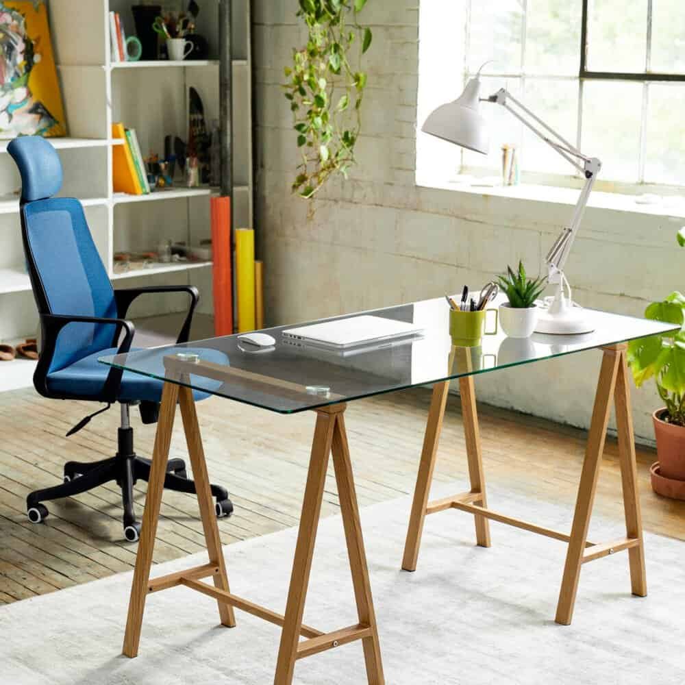 Alt text: Scrivania in vetro e legno con lampada da scrivania e piante in ufficio luminoso.