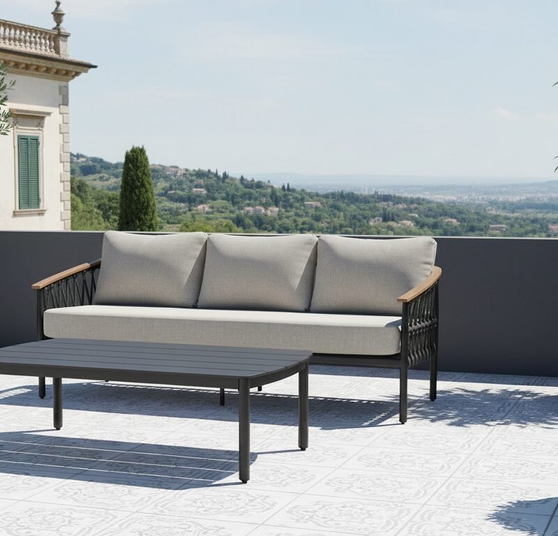 Outdoor rooftop terrace with a light gray cushioned sofa, matching coffee table, and potted trees against a scenic hillside view