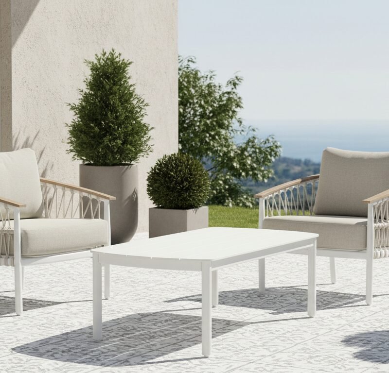 White outdoor seating area with two cushioned chairs and a low table on a patterned patio, overlooking the sea.