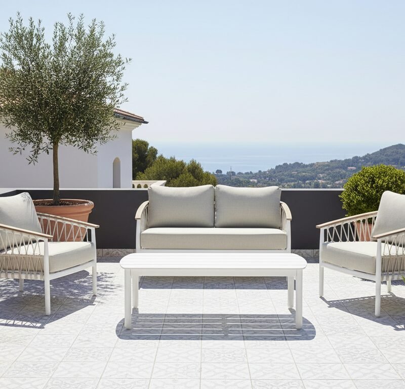 Outdoor terrace with white cushioned seating set and coffee table, potted trees, and a coastal view in the distance