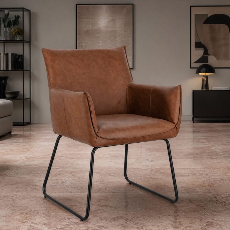 Brown leather lounge chair with metal legs in a modern living room with plants, art on the walls, and a black shelving unit in the background.