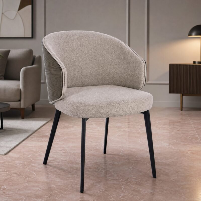 Beige upholstered chair with black legs in a modern living room, pink marble floor and a dark wood sideboard with a black lamp in the background.