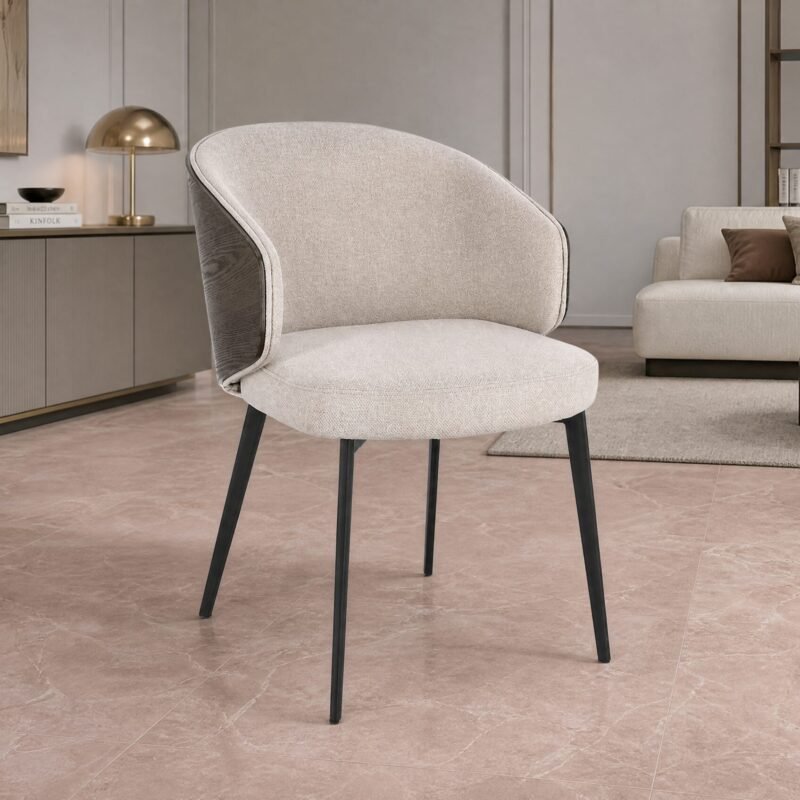 Beige curved-armchair in a modern living room with a cream sofa, brown cushions, and gold-accent shelving in the background.