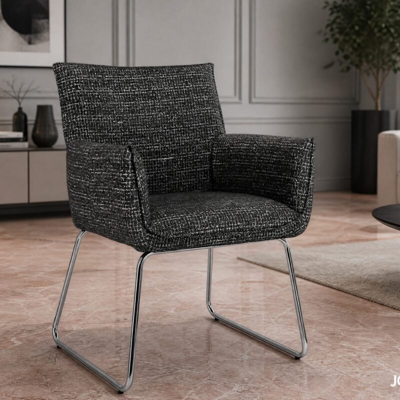 Modern living room with a black-and-white speckled upholstered chair on metal legs, beside a round black coffee table and plant-splashed backdrop.