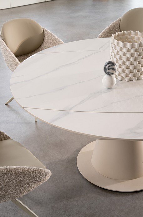 TAV ALJAMI 160X102-160 CREMA-STATUARIO8 - JOLLYGIUNCO Round white marble dining table with a pedestal base, surrounded by beige boucle chairs and a textured white vase centerpiece.