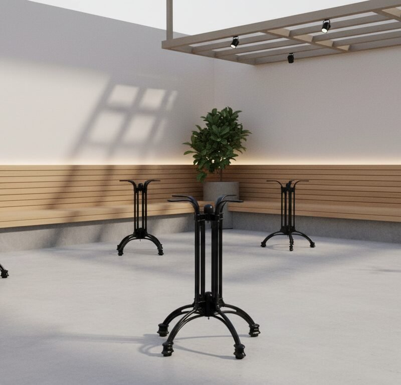 Empty outdoor patio with four black pedestal tables, long wooden benches along the walls, and potted plants under a skylight. Shadows cast on a light floor.