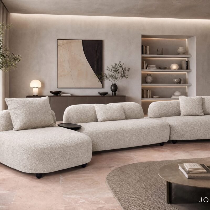Neutral living room with a large beige sectional, round coffee table, and built-in lit shelves.