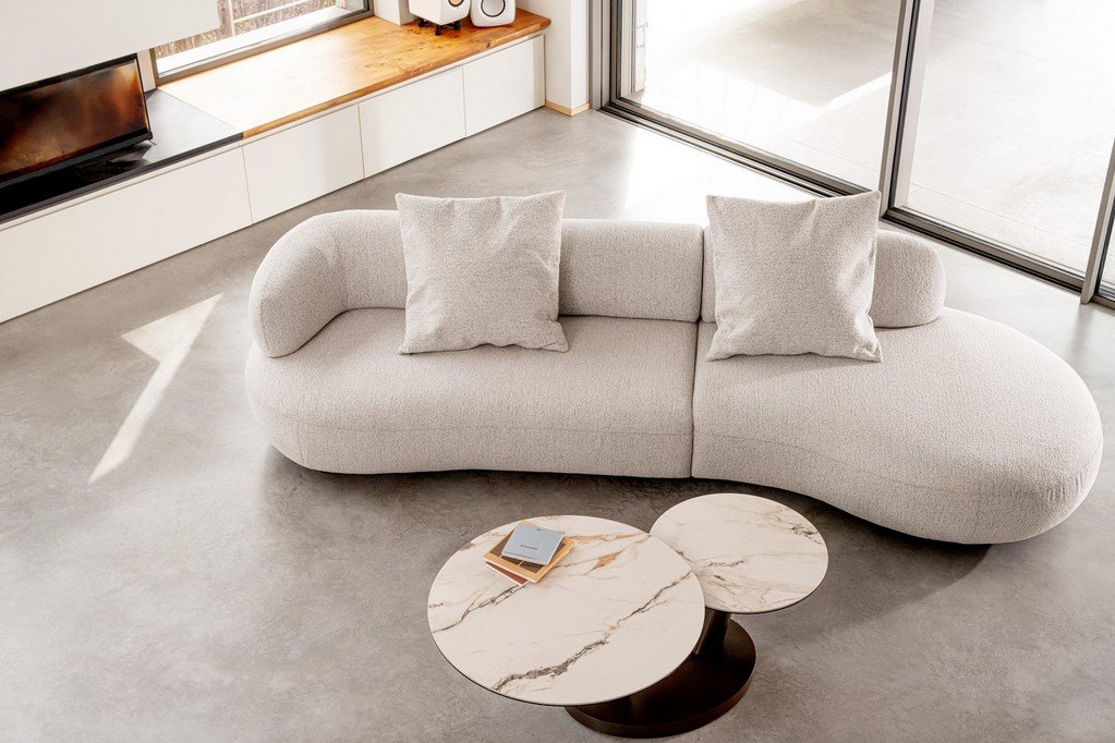 DIVANO C-C AFRODITE14 - JOLLYGIUNCO Contemporary living room with a curved light-gray sofa and two round marble-top coffee tables by large windows.