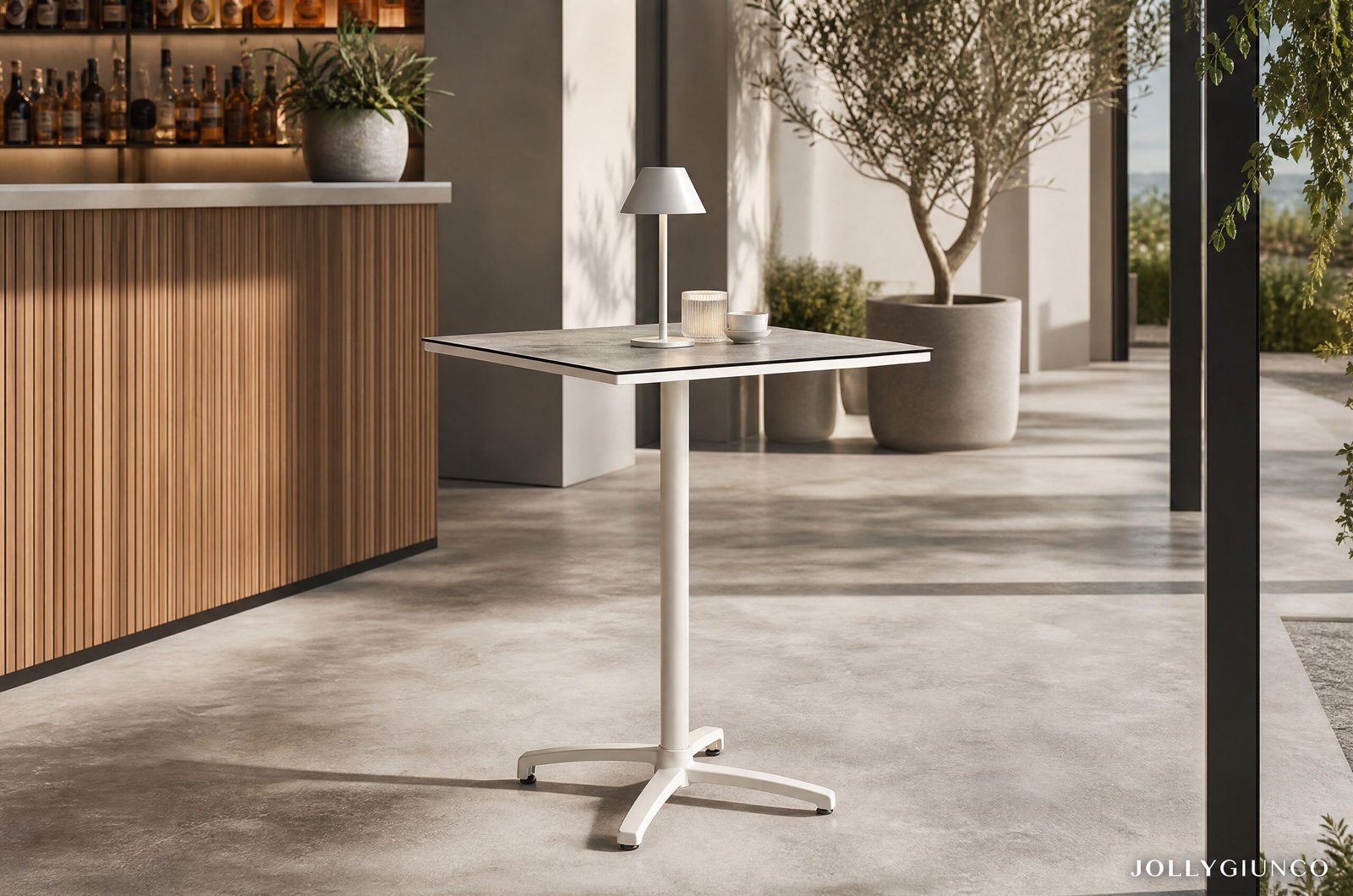 TAVOLO BAR ALTO CLARET 70X7010 - JOLLYGIUNCO Minimalist indoor lounge with a small white adjustable-height pedestal table, lamp, glass and cup, a wooden slat bar on the left, and potted plants by large windows.