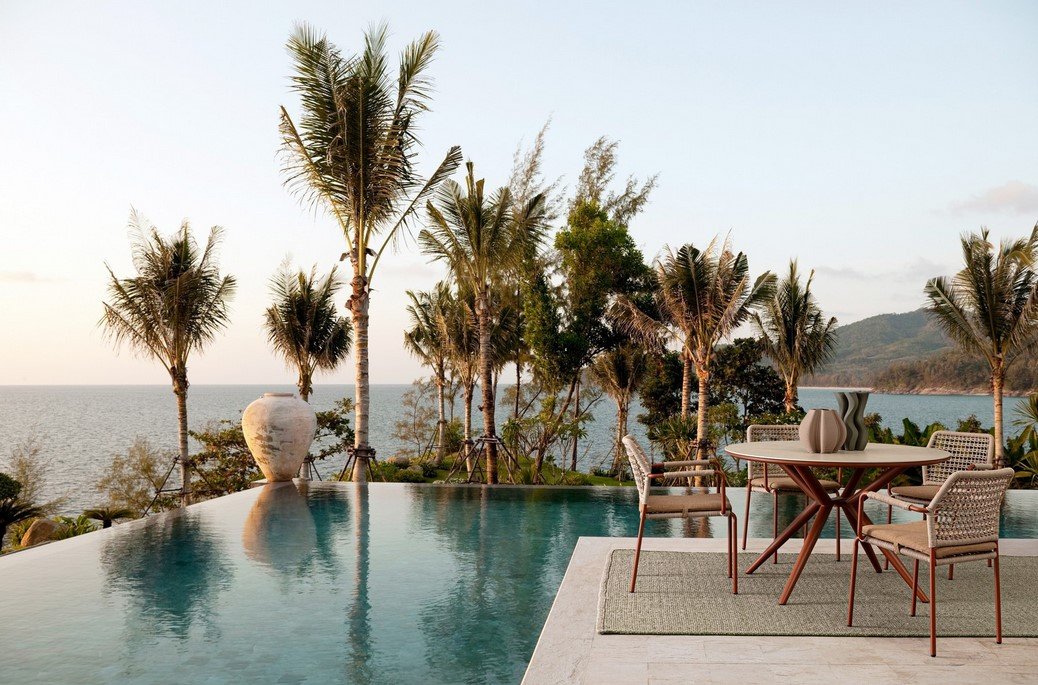 TAVOLO CABAS D120 RAME11 - JOLLYGIUNCO Infinity pool with ocean view, palm trees, and a round dining table with four chairs on a patio rug.