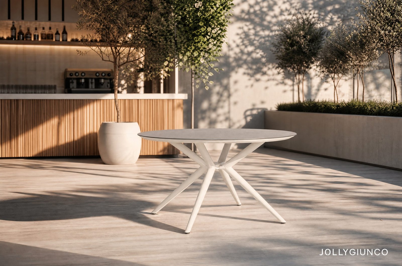 TAVOLO CABAS D13010 - JOLLYGIUNCO Outdoor patio scene with a round white table, wooden bar counter, potted tree, and greenery; watermark 'JOLLYGIUNCO' in the corner.