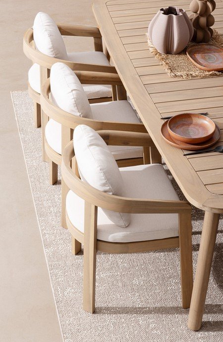 TAVOLO PABLO 240X1005 - JOLLYGIUNCO Light wood dining table with curved-back chairs and white cushions on a beige rug, in an outdoor-style setting.
